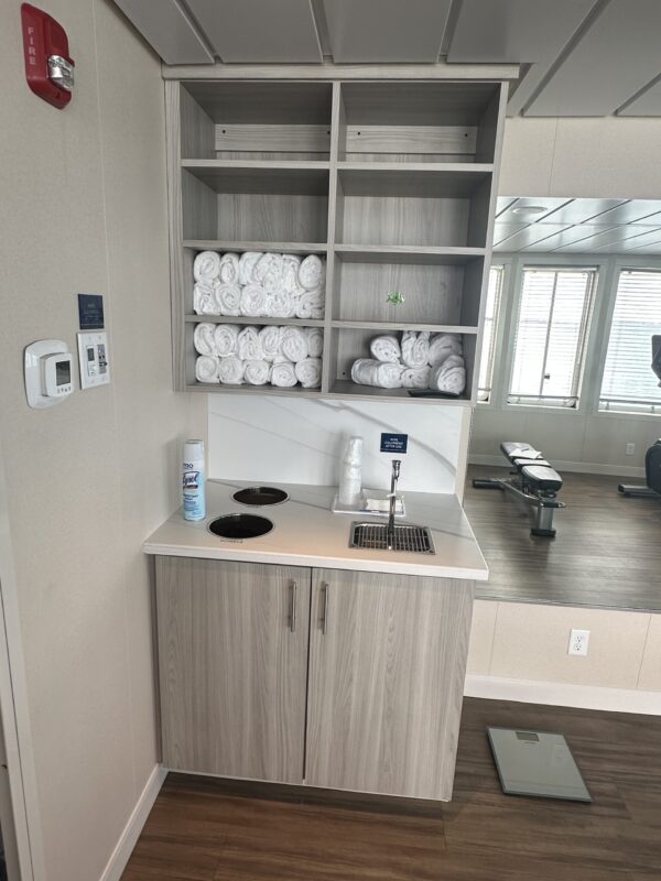 Grey base cabinet and wall shelving with water bottle fill station and towels