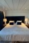 Large bed with dark blue brushed velvet headboard and matching pillows, white sheets