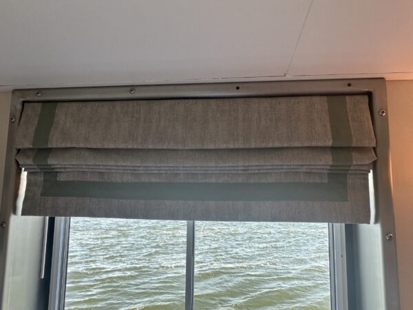 Light brown roman shades folded up with a window view of water