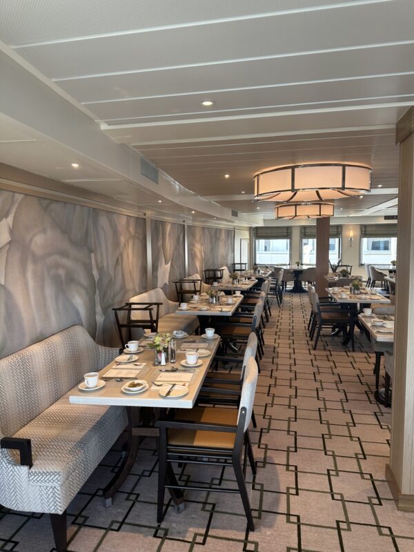 Full length view of dining room with tables settees chairs and place settings, patterned carpet and view to back windows