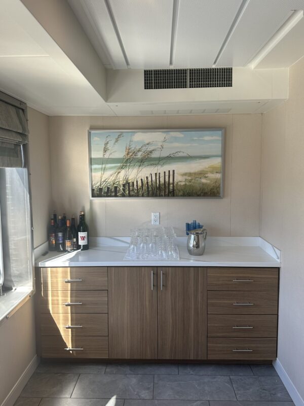 Servers corner with framed beachscape painting and several wine bottles next to window